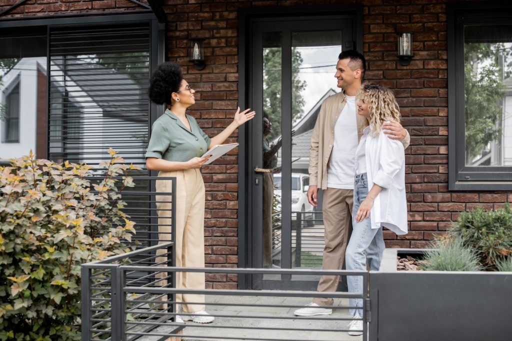 positive african american property realtor with folder showing contemporary cottage to happy owners